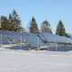 Solar panels in a snowy field with evergreen trees in the background.